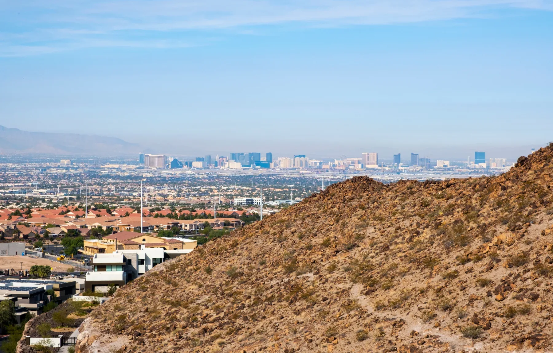 Aerial view of a desert hillside landscape with residential homes and sprawling city skyline in the distance, showcasing terr