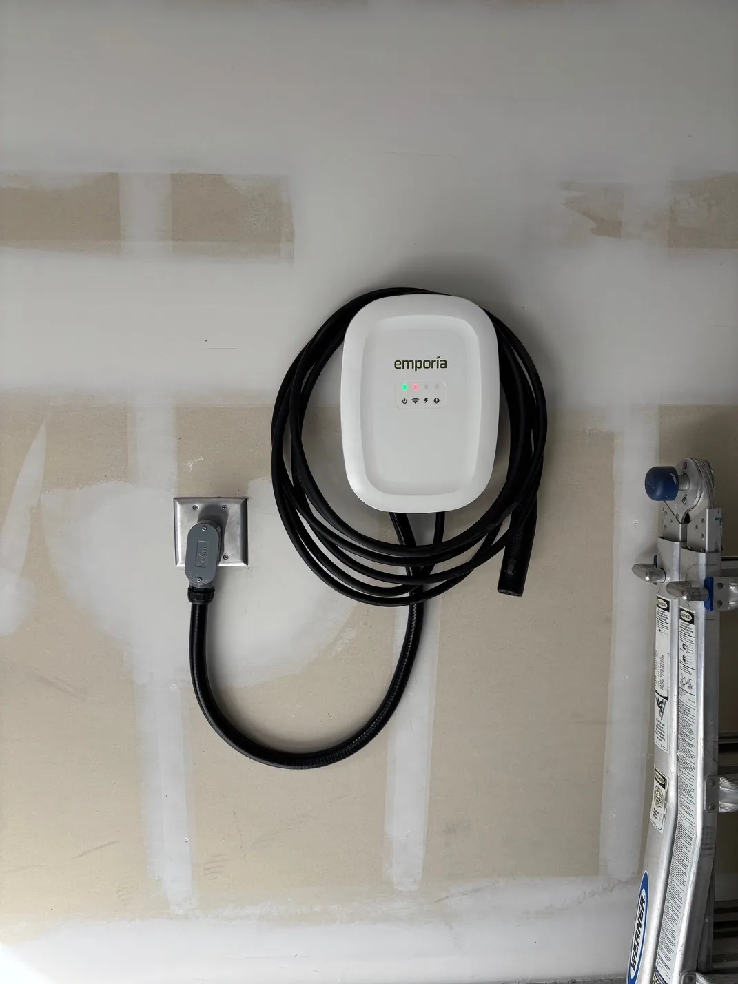 Emporia electric vehicle charging station mounted on drywall with coiled black cable.